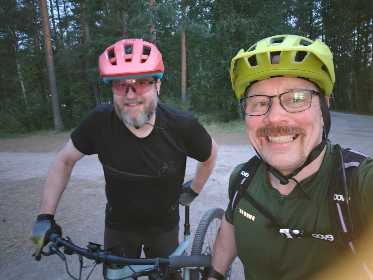 Tommi sinipinkissä kypärässä vasemmalla ja Jarkko keltaisessa oikealla, pyörien takana hiekkatiellä illan hämärässä